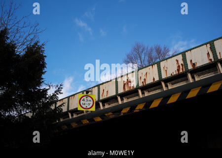 Una chiusura di un arrugginito road attraversando il ponte ferroviario di altezza con cartelli di avvertimento contro un cielo blu. Foto Stock