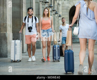 Le persone felici turisti tenendo a piedi e trascinando i bagagli in città per le vacanze Foto Stock