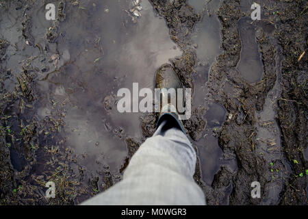 Un welly boot su fondi fangosi percorso impregnato d'acqua. Con il cielo riflesso nella pozza d'acqua. Foto Stock