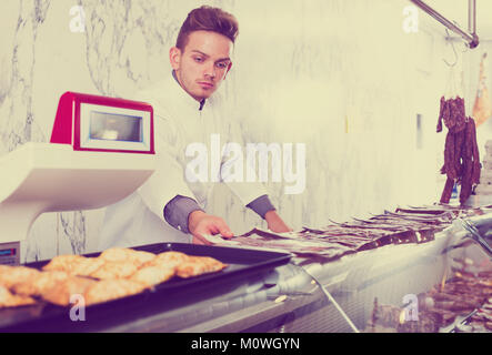 Giovani shop assistant in camice bianco al negozio di alimentari che mostra le carni fresche Foto Stock