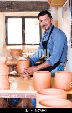 Sorridente uomo anziano rendendo pot con ruota di ceramiche in studio Foto Stock