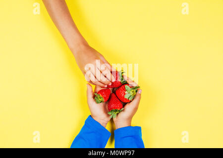 Kid mano tenendo fragola da un altro bambino con le mani in mano Foto Stock