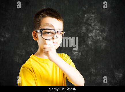 Ragazzo che guarda attraverso gli occhiali e lente di ingrandimento contro uno sfondo scuro Foto Stock