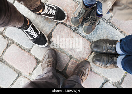 Piedi di uomo, donna, ragazzo e bambino. La famiglia reale si erge insieme in cerchio sulla strada di ciottoli. Vista superiore Foto Stock