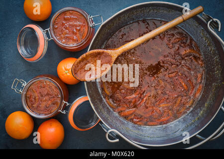 Pentola grande di marmellate fatte in casa e kilner giare con arance su un sfondo di ardesia Foto Stock