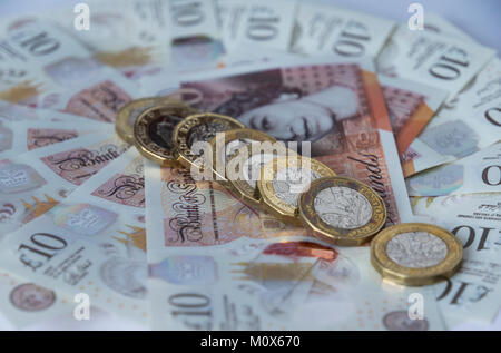 Una linea di nuovo British pound monete giacente in diagonale su una frontura circolare di nuovo polimero dieci Pound sterling note Foto Stock