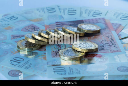 Diversi sterlina monete giacente su un letto circolare di nuovo dieci British pound note Foto Stock