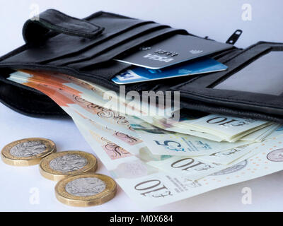 Un nero portafoglio in pelle contenente le carte di credito e di debito e carta moneta con tre monete cancelletto in primo piano Foto Stock