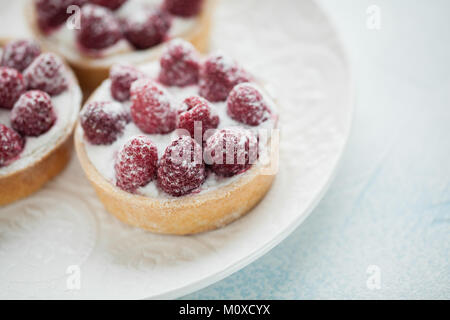 Deliziosi pasticcini di lampone su un bianco piastra vintage. Dolce trattare su un fondo azzurro. Foto Stock