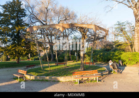 Giovane rilassante su un banco di lavoro presso il vecchio bandstand coperto di glicine di Giardini Pubblici, Venezia, Veneto, Italia in un raggio di golden luce della sera Foto Stock