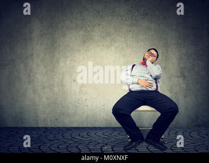 Giovani chunky uomo seduto in modo folle su una sedia e sognare riluttanti a lavorare. Foto Stock