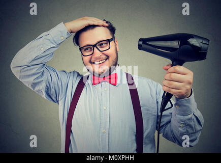 Giovane uomo chunky in abito formale con asciugacapelli per lo stile dei capelli mentre si posa sul grigio. Foto Stock