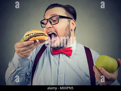 Paffuto uomo in occhiali mangiare hamburger scegliendo il cibo spazzatura invece di una dieta salutare. Foto Stock