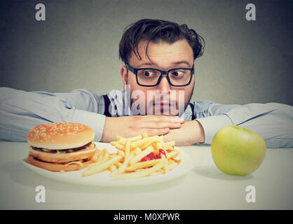 Giovane uomo chunky che vogliono allettante burger invece di una sana apple alla ricerca in questione. Foto Stock