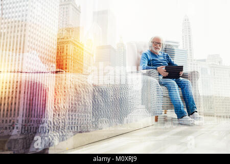 Felice l'uomo senior utilizzando i suoi gadget moderno e sorridendo allegramente Foto Stock