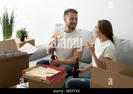 Felici proprietari di casa mangiare formaggio pizza bere birra celebrando h Foto Stock