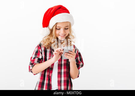 Ritratto di un simpatico bambina vestito di natale hat tramite telefono cellulare isolato su sfondo bianco Foto Stock