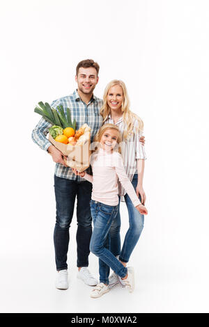 A piena lunghezza Ritratto di una famiglia felice tenendo la carta shopping bag piena di negozi di generi alimentari mentre in piedi e guardando la telecamera isolato su bianco backgroun Foto Stock