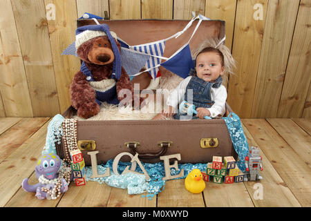 3 mese vecchia razza mista baby boy giocando in toy box vintage valigia piena di giocattoli Foto Stock