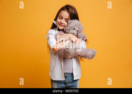 Immagine di allegro bambina bambino in piedi isolato su sfondo giallo azienda giocattolo orsacchiotto in mani. Gli occhi chiusi. Foto Stock