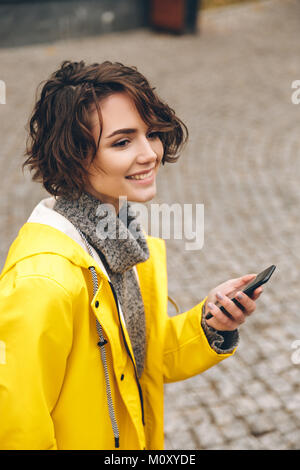 Ritratto di bella bruna femmina camminando sul selciato tenendo lo smartphone nel lato alimentazione a scorrimento nella rete sociale Foto Stock