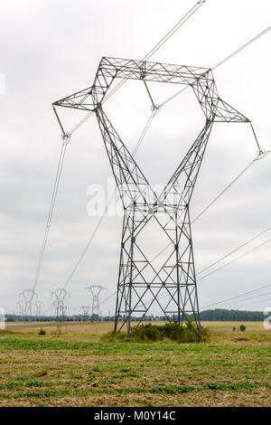 Una torre di trasmissione nel mezzo di un campo arato il supporto di linee ad alta tensione con decine e decine di altri pali elettrici in background sotto un clou Foto Stock