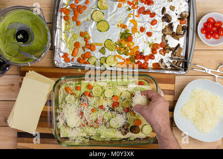 Lo chef prepara lasagna vegetale aggiungendo uno strato di formaggio grattugiato su i dadini di verdure e pasta visto dal di sopra Foto Stock