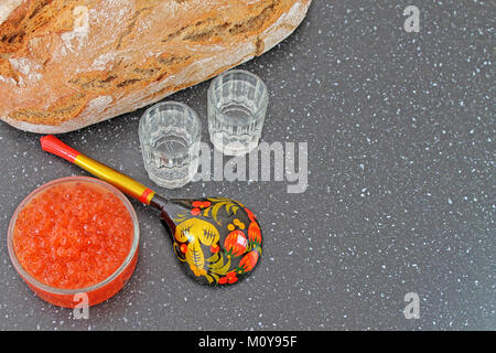 Caviale rosso in una ciotola e pane fresco. Cucchiaio di legno dipinta in stile tradizionale Khokhloma e colpo di vetro di vodka. Tradizionale cibo russo. Foto Stock