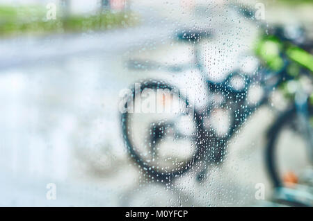 Vista delle biciclette parcheggiate attraverso il vetro con gocce di acqua Foto Stock