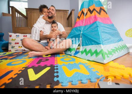 Padre seduto sul pavimento nella sala giochi holding figlio e figlia Foto Stock