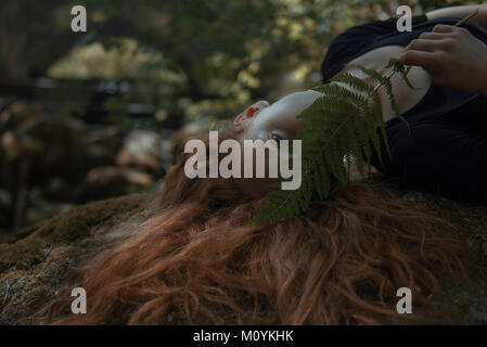 Caucasian donna con capelli rossi nasconde la faccia dietro leaf Foto Stock