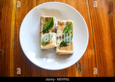 Colazione minimalista di toast, formaggio di capra, le fette di pomodoro condito con basilico tailandese disposti in piccoli quadrati Foto Stock