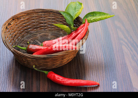 Peperone rosso con foglie in un piccolo cesto in vimini Foto Stock