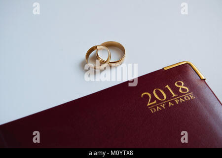 Pianificazione di un matrimonio in 2018. Vista superiore del 2018 personal organizer e due anelli di nozze su sfondo bianco con spazio per il testo. Nuovo concetto di vita Foto Stock
