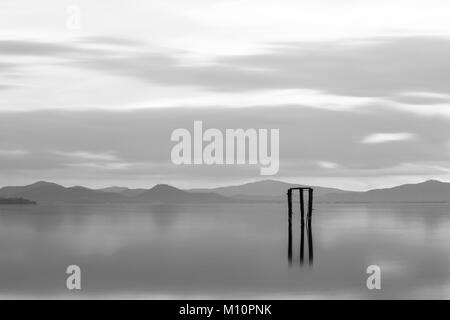 Una visione minimalista del lago Trasimeno al tramonto, con luce tenue e di toni e pali in primo piano, riflettendo sull'acqua Foto Stock