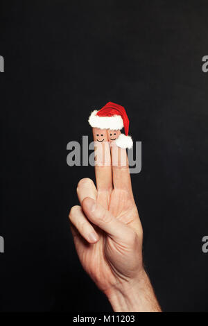 Coppia di natale. Due Felice Natale faccia dita in cappelli di Babbo Natale sul background Blackboard Foto Stock