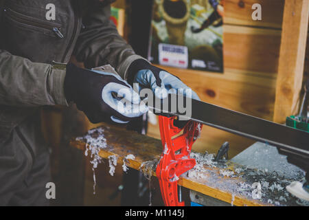 Un lavoratore di sesso maschile in un servizio sci riparazioni in officina la superficie di scorrimento dello sci. Close-up di una mano con una lottatrice di plastica per la rimozione di cera, rimozione Foto Stock