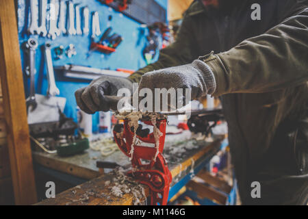 Un lavoratore di sesso maschile in un servizio sci riparazioni in officina la superficie di scorrimento dello sci. Close-up di una mano con una lottatrice di plastica per la rimozione di cera, rimozione Foto Stock