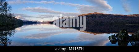 Vista panoramica di un maestoso Coniston Water. Nuvole e sole-baciato fells perfettamente riflessa nell'acqua ancora Foto Stock