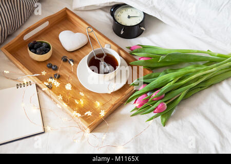 Un vassoio con tè e pan di zenzero a forma di cuore e un mazzo di tulipani sul letto Foto Stock