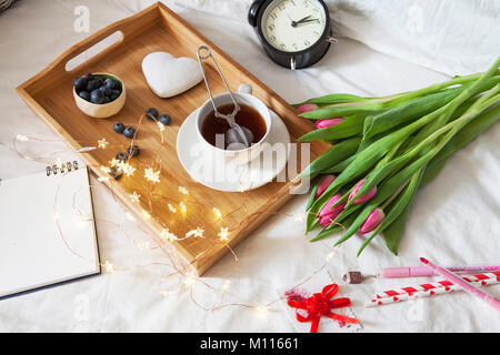 Un vassoio con tè e pan di zenzero a forma di cuore e un mazzo di tulipani sul letto Foto Stock