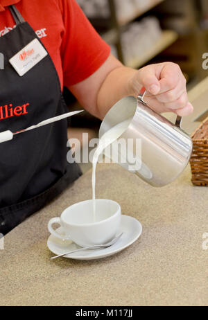 Latte caldo versando in una tazza di caffè a Hillier garden centre cafe. Foto Stock