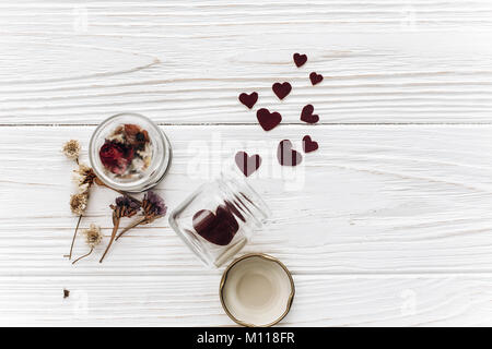 Elegante cuori nel vasetto di vetro e rose bianche su sfondo di legno. insolito happy valentines day concetto. biglietto di auguri laici piatta con spazio per il testo. Foto Stock