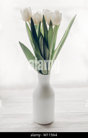 Eleganti tulipani bianco in stile minimalista di moda vaso a rustico in legno davanzale in morbida luce mattutina. ciao molla concetto, spazio per il testo Foto Stock