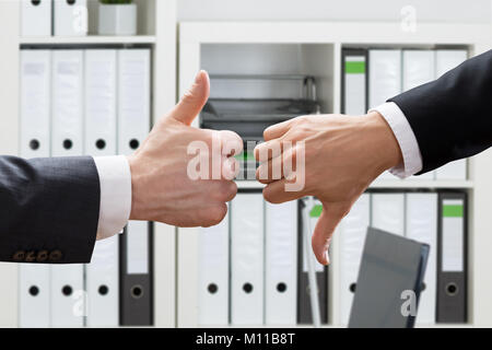 Close-up di business man mano che mostra i pollici in su e in giù in ufficio Foto Stock