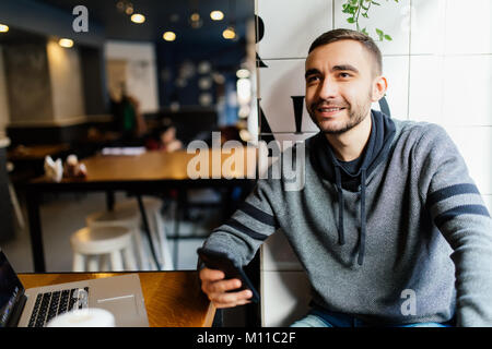 Close-up dei maschi di mani e utilizzando i moderni smart phone in cafe shop. Uomo di inviare i nuovi messaggi su moderne smart phone. Foto Stock