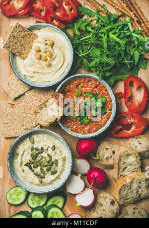 Vegano scheda snack. Flat-laici di varie salse vegetariano hummus, babaganush e muhammara con cracker, pane e verdure fresche, vista dall'alto. Pulire mangiare Foto Stock