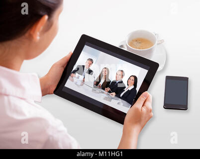 Imprenditrice Video Conferenza sulla tavoletta digitale con la tazza di tè sulla scrivania Foto Stock