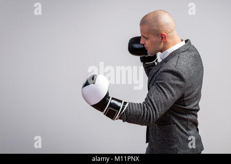 Giovane uomo calvo, fiducioso business man in maglia bianca, grigio tuta e guantoni da pugilato facendo un uppercut, boxe bianco su sfondo isolato, vista laterale Foto Stock