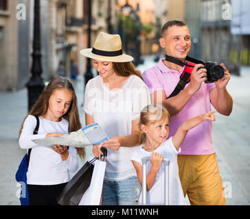 Felice allegra famiglia turistiche usando la mappa e prendendo foto della città passeggiando con telecamera e telefono Foto Stock